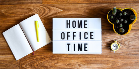 lightbox with text HOME OFFICE TIME in front wooden background with cacrus alarm clock and notebook with pen copy space, banner for freelance coronavirus covid-19 quarantine isolation