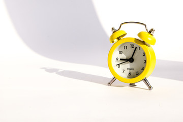 Yellow alarm clock with large shadow on white background, copy space