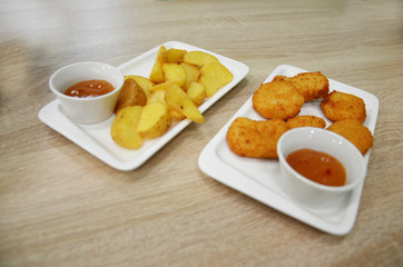 Wall Mural - chicken nuggets and fried potatoes on a white plate on a table in a cafe or restaurant