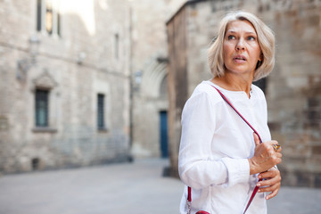 Wall Mural - Elegant mature woman is posing in time walking on the street of old city