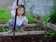 © Sirichai - A cute Asian girl helping her family to grow vegetables in their backyard, using a spade to dig up the soil, preparing it for sowing.