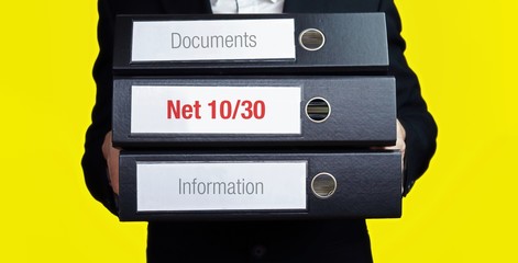 Net 10/30 – finance/economics. Man carries a stack of 3 file folders. A folder has the label Net 10/30. Business, statistics concept