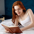 © Dmitrii Kotin - Redhead woman lying and relax on the bed and looks in her diary.