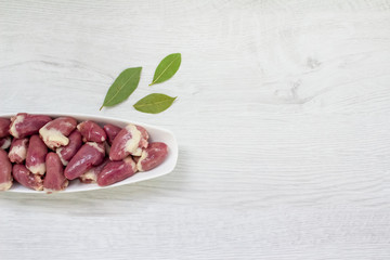 Wall Mural - Top view on raw chicken hearts in blue bowl with aromatic spices, bay leaves and peppercorns, on white wooden background with copy space