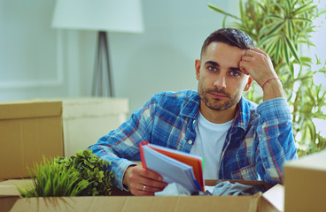 A moving man sitting on the floor in empty apartment, Among the Boxes, Checking the List of Things