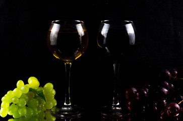 Grapes are on the table. Next to it are two glasses in which red and white wine is poured