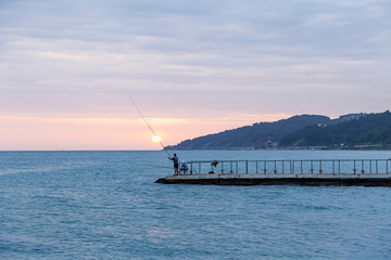 two men catch fish from a pier in the black sea at sunset