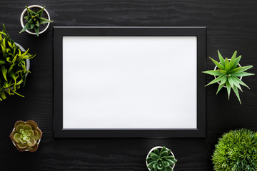 Wall Mural - Black desk with green plants. Mockup frame in the middle.