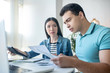 © zinkevych - Brunette male and dark-haired female sitting at desk, checking papers