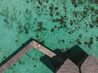 Wall Mural - Aerial view of  couple lying on wooden pier in tropical resort with aqua mint ocean. Couple on wooden brown jetty on calm relaxing, top view