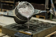 Metal sand casting technique pouring molten aluminum silver colored liquid into a mold in a induastrial environment, workshop space