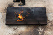 A man holding a fire torch and burning a big piece of oak creating flames and smoke, old Japanese shou sugi ban technique. black wooden material. Grain, texture