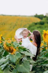 Wall Mural - Happy mother with the little daughter in the field of sunflowers. mom and baby girl in mom's hat having fun outdoors. family concept. mother's, baby's day. summer holiday