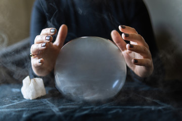 Fortune teller holds hands above magic crystal ball with smoke around. Conceptual image of black magic and occultism