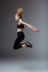 Wall Mural - side view of curly woman in sportswear jumping on grey