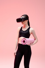 Wall Mural - sportswoman in virtual reality headset holding fitness mat on pink