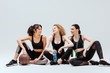 © LIGHTFIELD STUDIOS - happy multicultural girls sitting with sport equipment on white