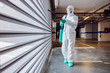 Full length of worker in sterile protective suit and mask sterilizing door of a garage from corona virus / covid-19.