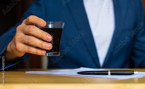 Close-up of the hands of a well-dressed man in a blue suit and a white shirt drinking a glass of coffee on a desk Tableau sur Toile