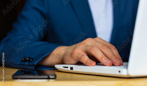 Photographie Close-up of the hands of a well-dressed man in a blue suit and a white shirt using a laptop at a desk