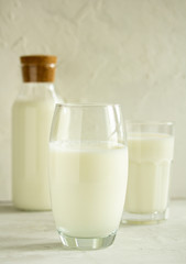 Wall Mural - Milk in a transparent glass on a light gray background on the background of a bottle with milk and a glass with milk