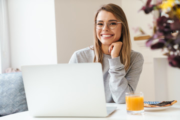 Wall Mural - Photo of cheerful young woman using laptop while having breakfast