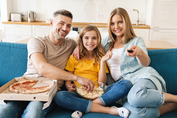 Wall Mural - Photo of cheerful family eating popcorn and pizza while watching tv