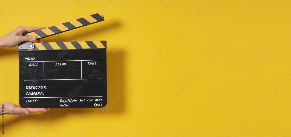 Hand is holding clapper board or movie slate.It is used in video production and film industry on yellow background. - obrazy, fototapety, plakaty 