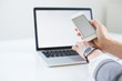 © Dominika - Close-up of smartphone with blank screen in hands of young woman sitting at white table and touching screen. On table laptop with blank screen. White style. Minimalism. Mock up,space for ad
