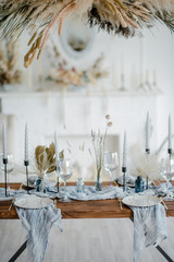 Stylish table setting with dried flowers. Plate with vintage golden fork and knife, candles, dusty blue napkins on wooden table. Winter wedding decoration.