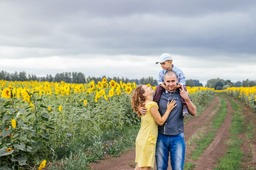 Wall Mural - A young family of 3 people walking in a field of sunflowers.