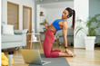 © Drazen - Young sportswoman vlogging about stretching exercises while using laptop at home.