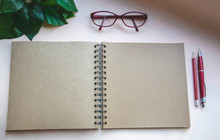 Top View Of Open Brown Spiral Notebook On Light Background With Pen, Pencil, Glasses And Green Leaves. Flat Lay, Creative Workspace Office. Business Or Education Concept With Copy Space.