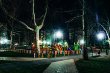 Night View Of A Colorful Playground Among Park Trees In A Residential Area Of Anapa. The Pine Park Is Lit By The Bright White Light Of The Lanterns.
