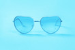 © taniasv - Blue trendy stylish and fashionable slightly heart shaped feminine sunglasses closeup on monochrome blue background with copy space. Zine summer and vacation minimal concept