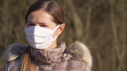 Wall Mural - Young woman in white cotton virus face mouth mask sitting in park, blurred trees background. Coronavirus covid-19 protection concept