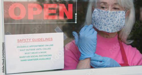 Cuadros en Lienzo With cautious optimism a mature small business owner wearing a face mask and disposable gloves posts safety rules as she reopens her store after the coronavirus shutdown