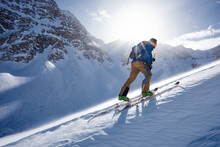 Man ski touring uphill in the wind and backlit by sun