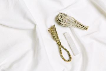 White sage bundle, sweetgrass braid, selenite crystal for smudging ritual on white natural canvas fabric