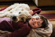 Boy And His Dog Cuddling On The Floor Together On A Blanket.