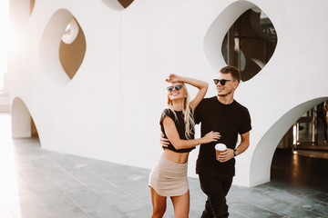 Newly wed couple on honeymoon enjoying time in the city. Guy jumping with joy blonde lady laughing in happiness. City view photography in cheese like wall building.