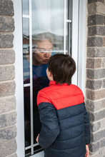 Young Boy Looking Through Window At Grandma During Covid 19 Pandemic.