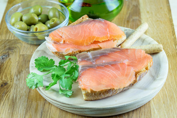 Wall Mural - Sandwiches with red fish salmon on the wooden plate, olives and olive oil closeup. Tasty mediterranean snack food.