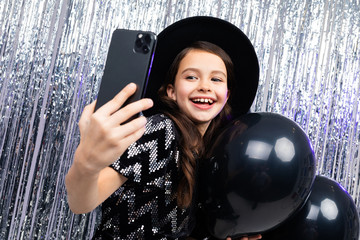 young girl on holiday takes a photo on a smartphone among black balloons on a shiny background