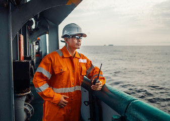 Filipino deck Officer on deck of vessel or ship , wearing PPE personal protective equipment. He holds VHF walkie-talkie radio in hands. Dream work at sea