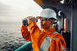 © Igor Kardasov - Filipino deck Officer on deck of vessel or ship , wearing PPE personal protective equipment. He is looking through binoculars.
