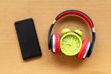 Fototapeta Konie - Headphones and alarm clock and smartphone on wooden desk. Musical concept