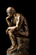 A bronze replica statue of Rodin's Thinker on a black marble background