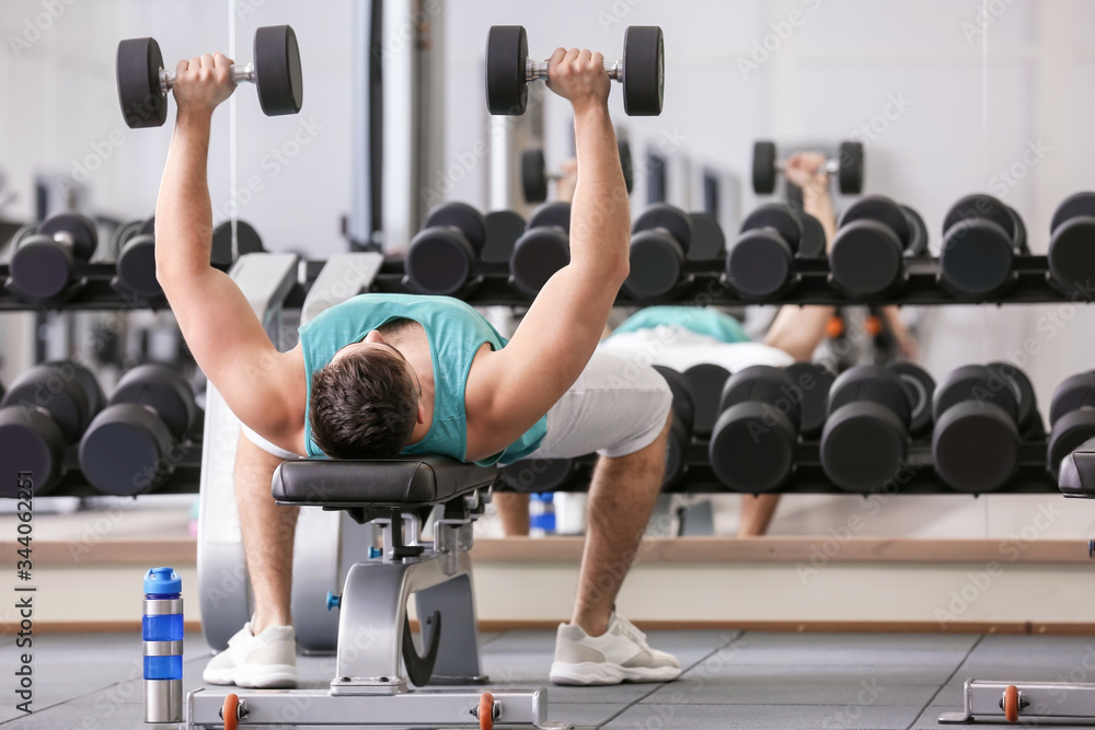 Sporty young man training with dumbbells in gym