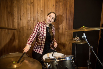 Professional drum set closeup. Beautiful young girl drummer in checkered shirt with drumsticks playing drums and cymbals, on the live country or rock music concert or in recording studio. Female drumm